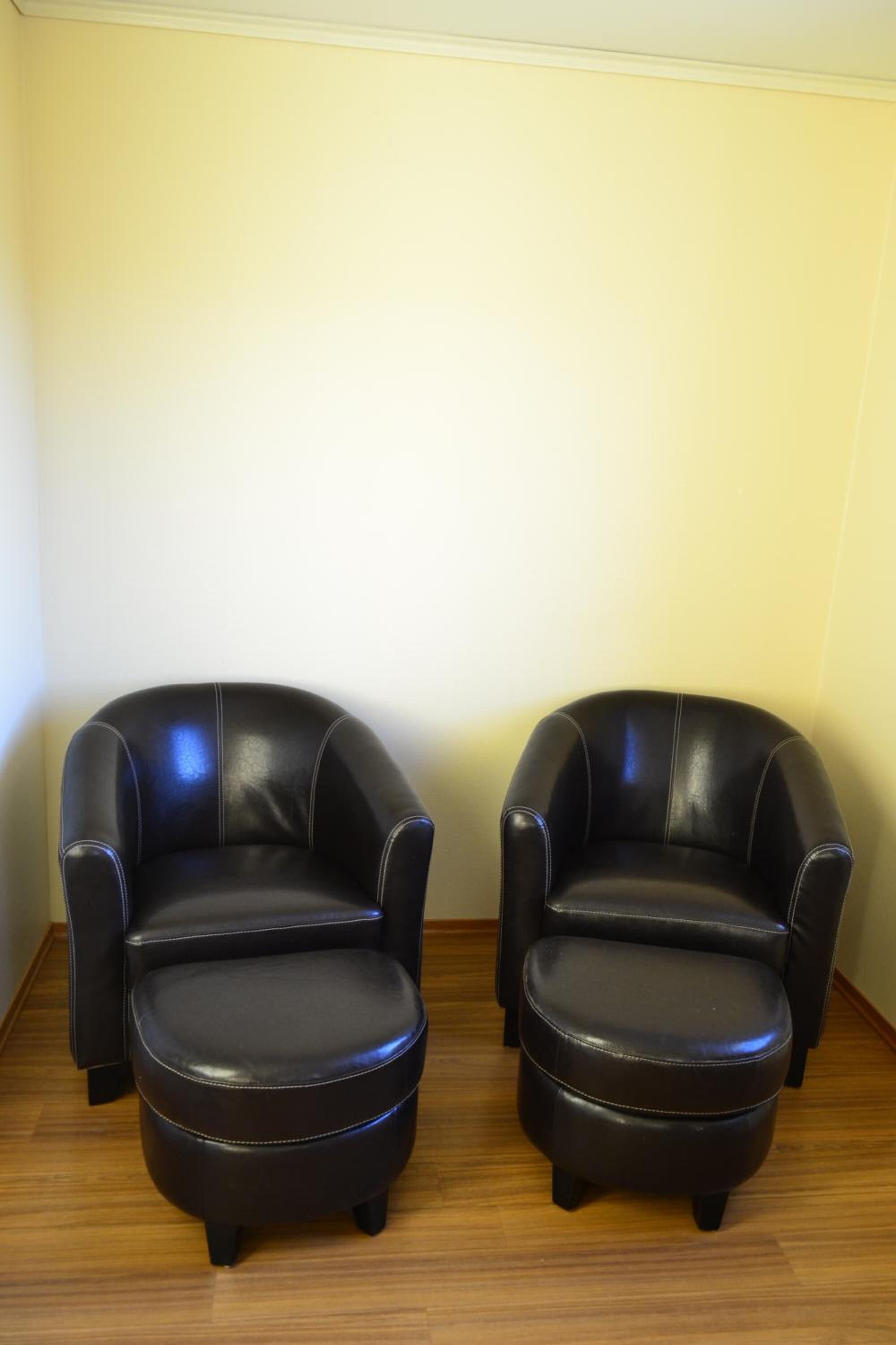 Two black leather armchairs with wooden legs, positioned against a plain wall on a wooden floor.