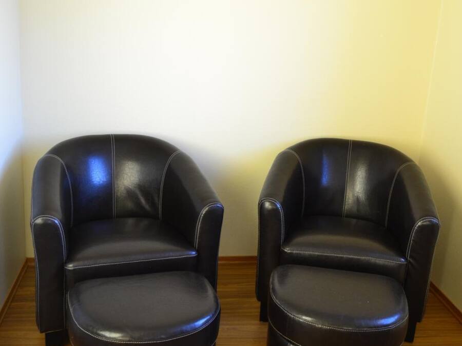 Two black leather armchairs with wooden legs, positioned against a plain wall on a wooden floor.