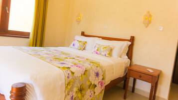 Una cama bien hecha con ropa de cama floral, una mesita de noche de madera con un control remoto y dos lámparas de pared.