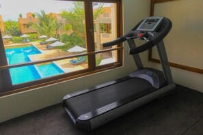A treadmill in a room with a window overlooking a pool area.