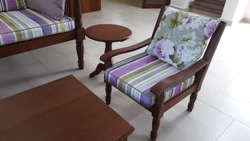 Una silla de madera con un cojín floral y uno a rayas, una mesita redonda pequeña y un banco de madera.
