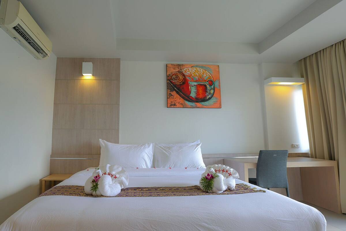 A hotel room with a neatly made bed, a painting on the wall, and a desk with a chair.