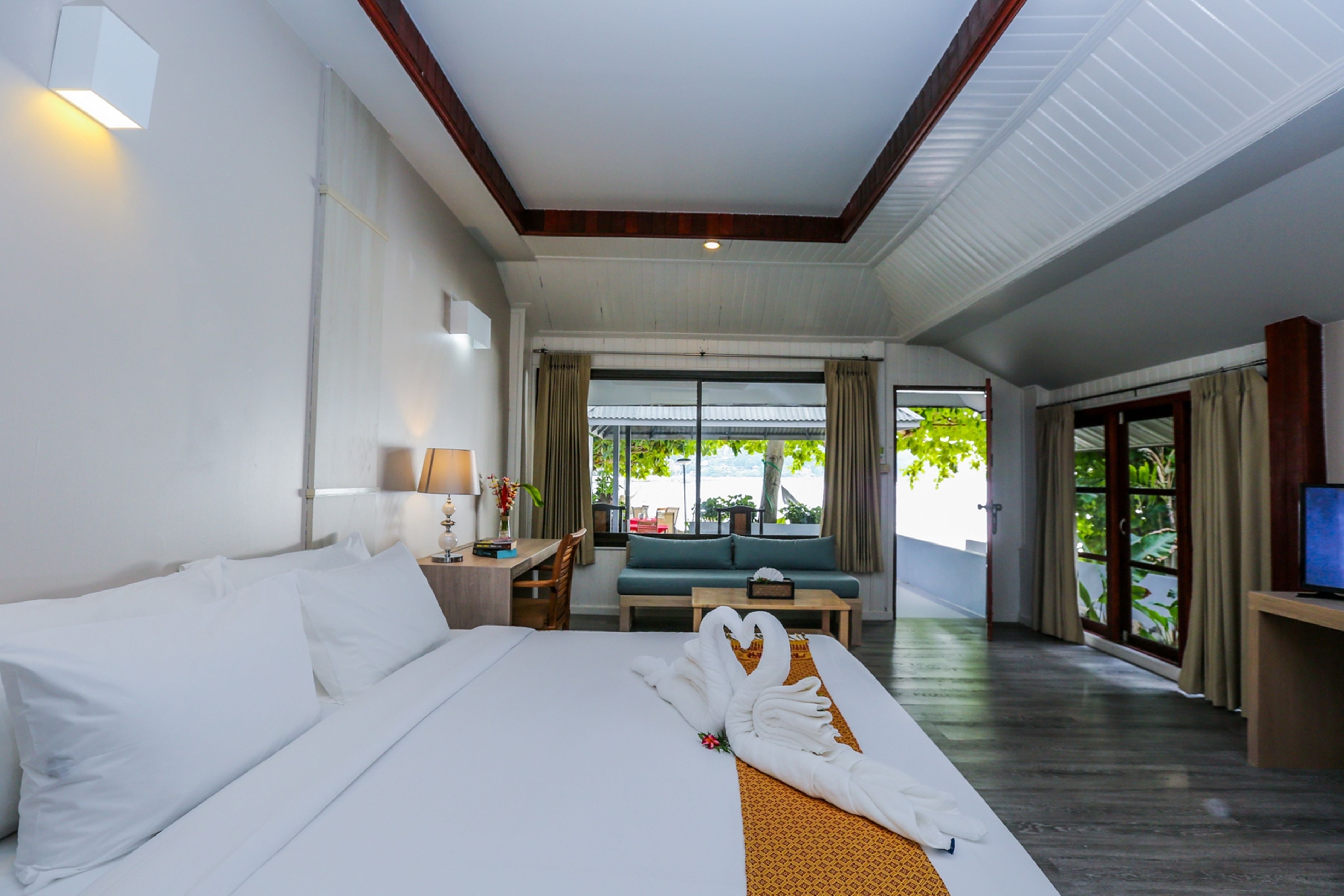 A hotel room with a large bed, a desk, a sofa, and a TV.