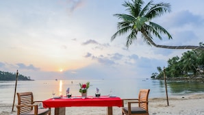 A table set for two on a beach with a red tablecloth, two wooden chairs, and a palm tree in the background. - Villa Cha Cha Salad Beach Koh Phangan (Ko Pha-ngan)