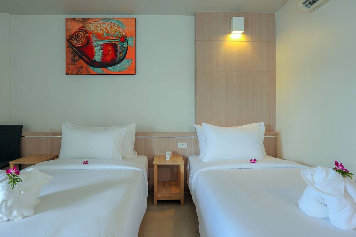 A hotel room with two beds, a painting on the wall, a chair, and a nightstand with a lamp.