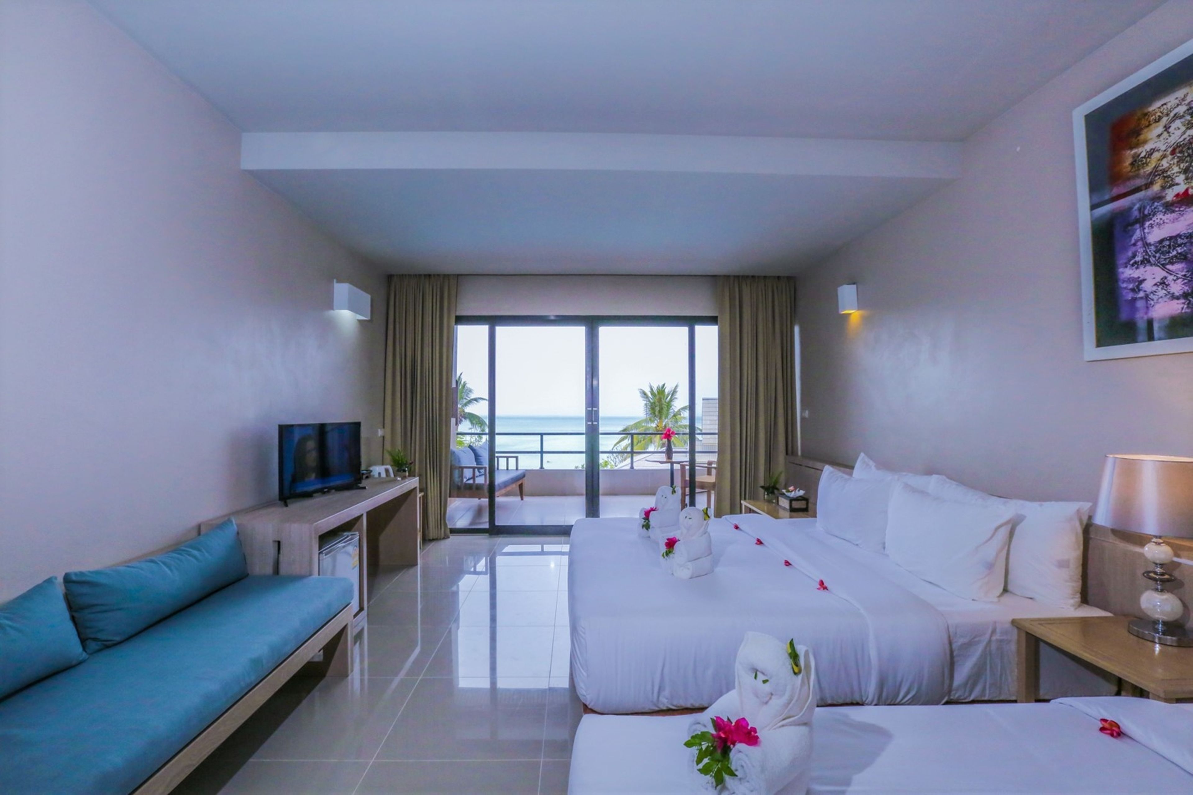 A hotel room with a balcony, a sofa, a bed, a TV, and a desk.