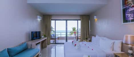 A hotel room with a balcony, a sofa, a bed, a TV, and a desk.