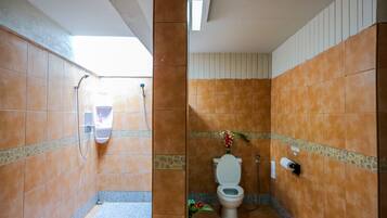 A bathroom with orange tiled walls, a white toilet, a hand dryer, and a small plant.