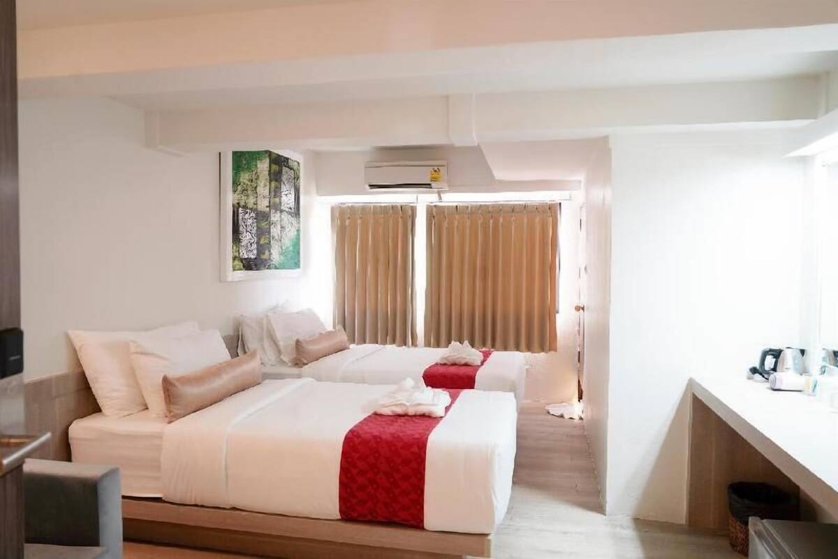 A hotel room with two beds, a desk, and a large window with curtains.