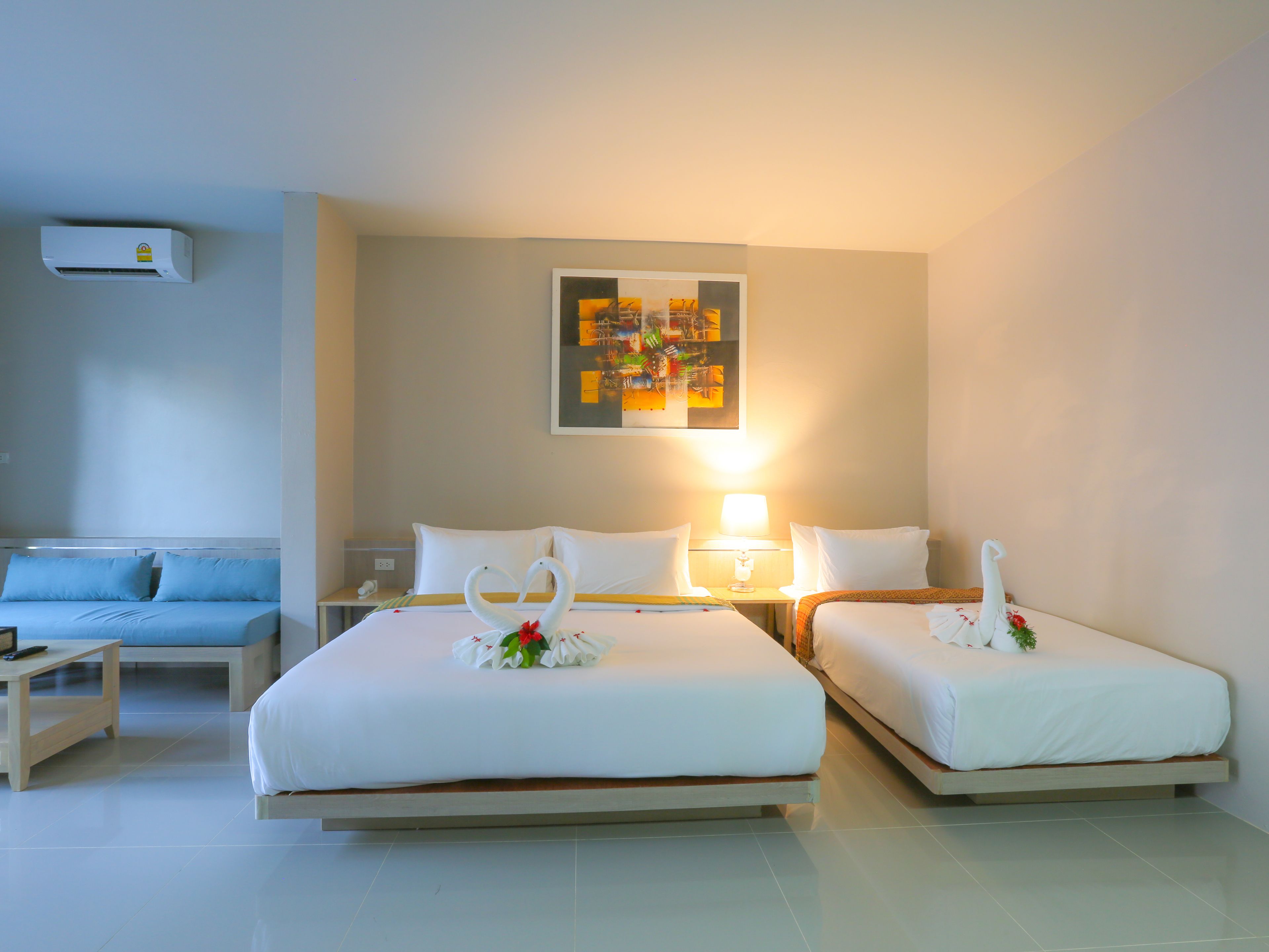 Habitación de hotel con dos camas, un sofá, una mesita de noche con lámpara y aire acondicionado de pared.