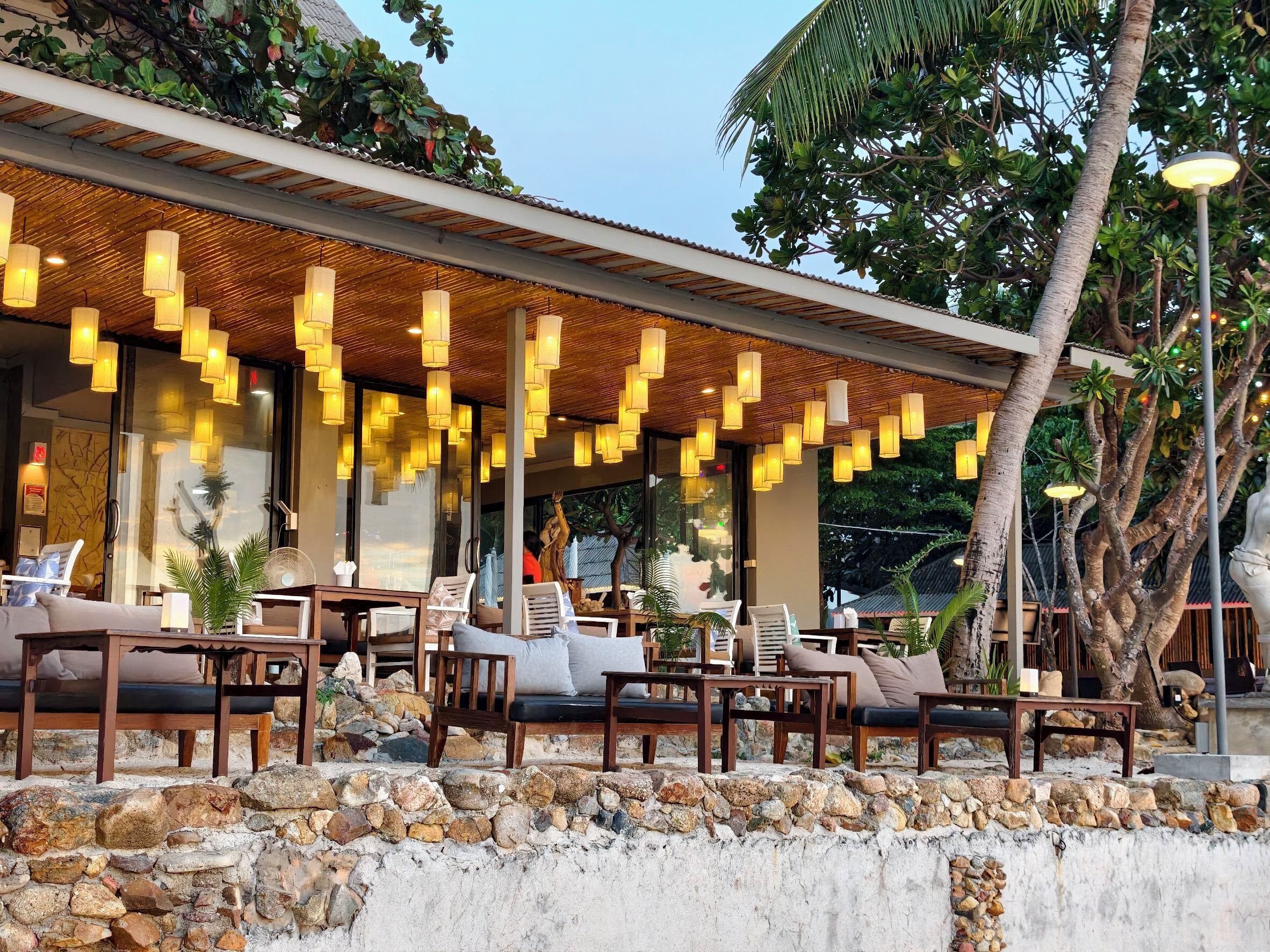 An outdoor seating area with stone walls, wooden furniture, and hanging lights.
