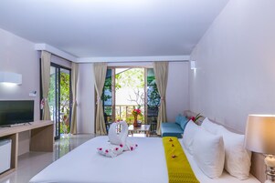 Habitación de hotel con cama, televisión, sofá y balcón con cortinas.