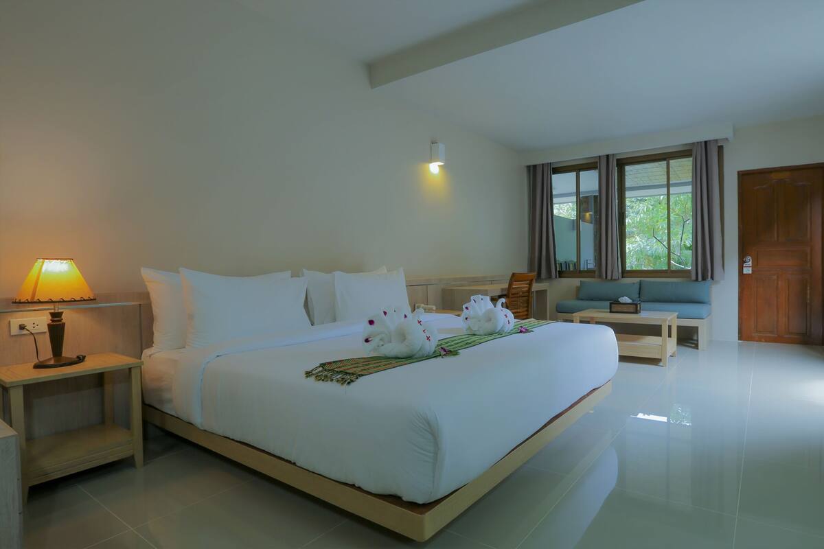 A neatly arranged bedroom with a bed, bedside table, lamp, and a sofa.