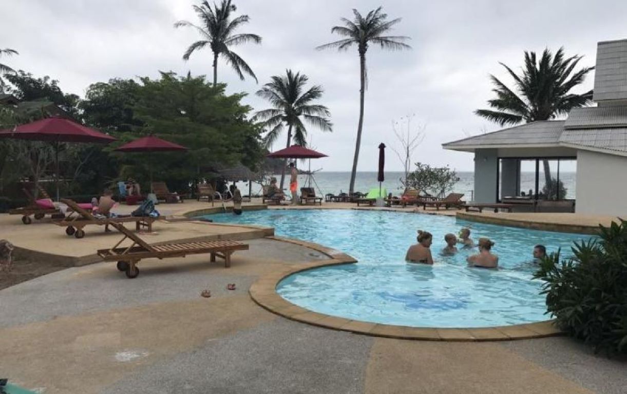 A pool area with lounge chairs and umbrellas, surrounded by palm trees and a building.