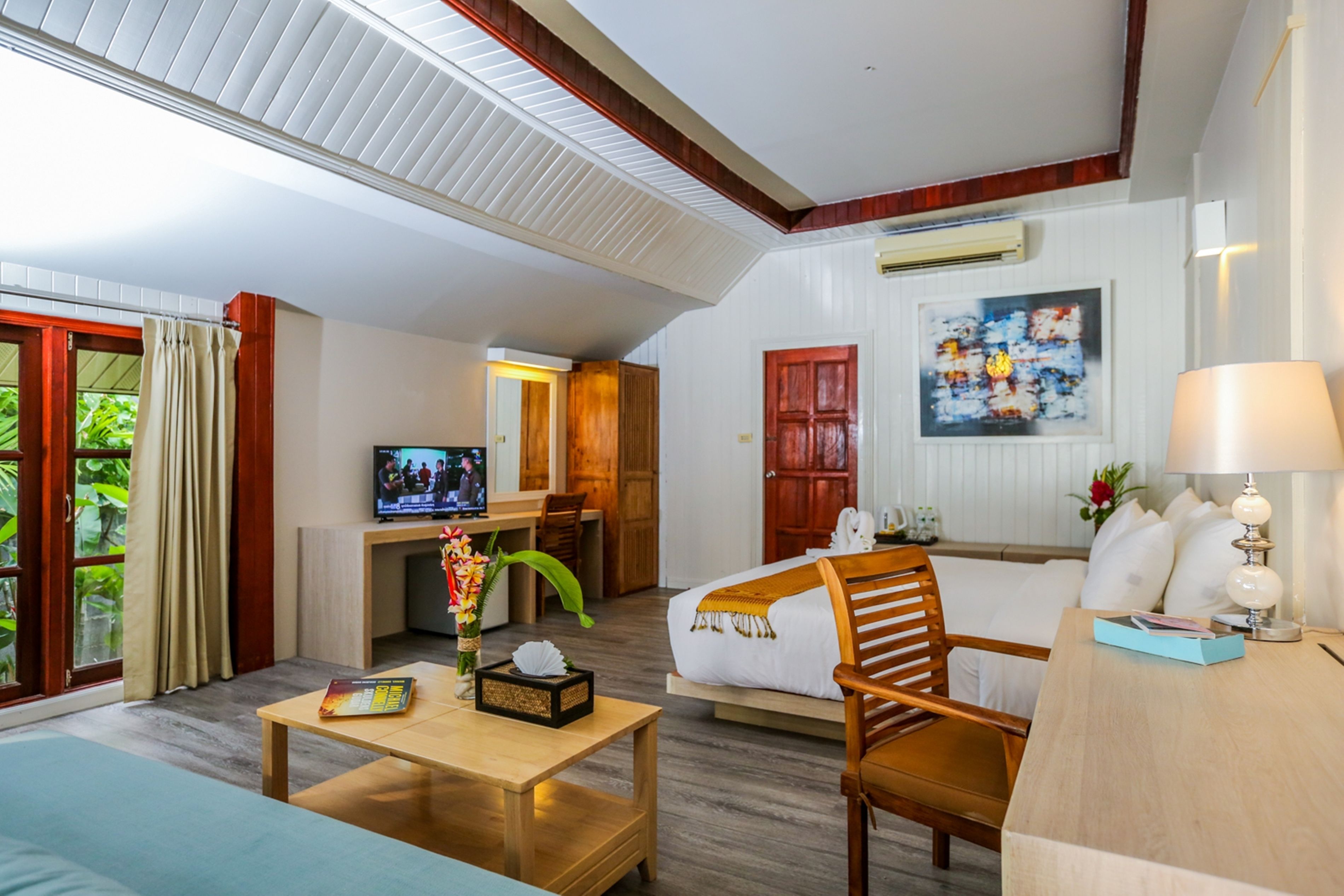 Habitación de hotel con cama, escritorio, televisor, sofá y ventana con cortinas.