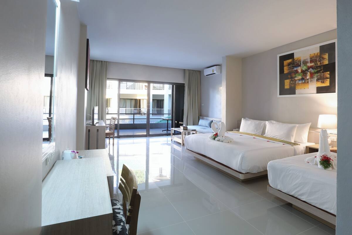 A hotel room with a bed, a desk, a chair, a balcony with a view, and a painting on the wall.
