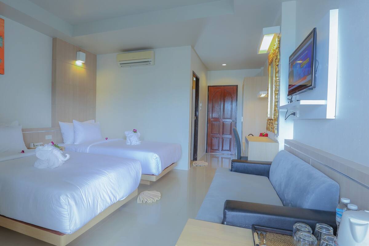 A hotel room with two beds, a sofa, a TV, and a painting on the wall.
