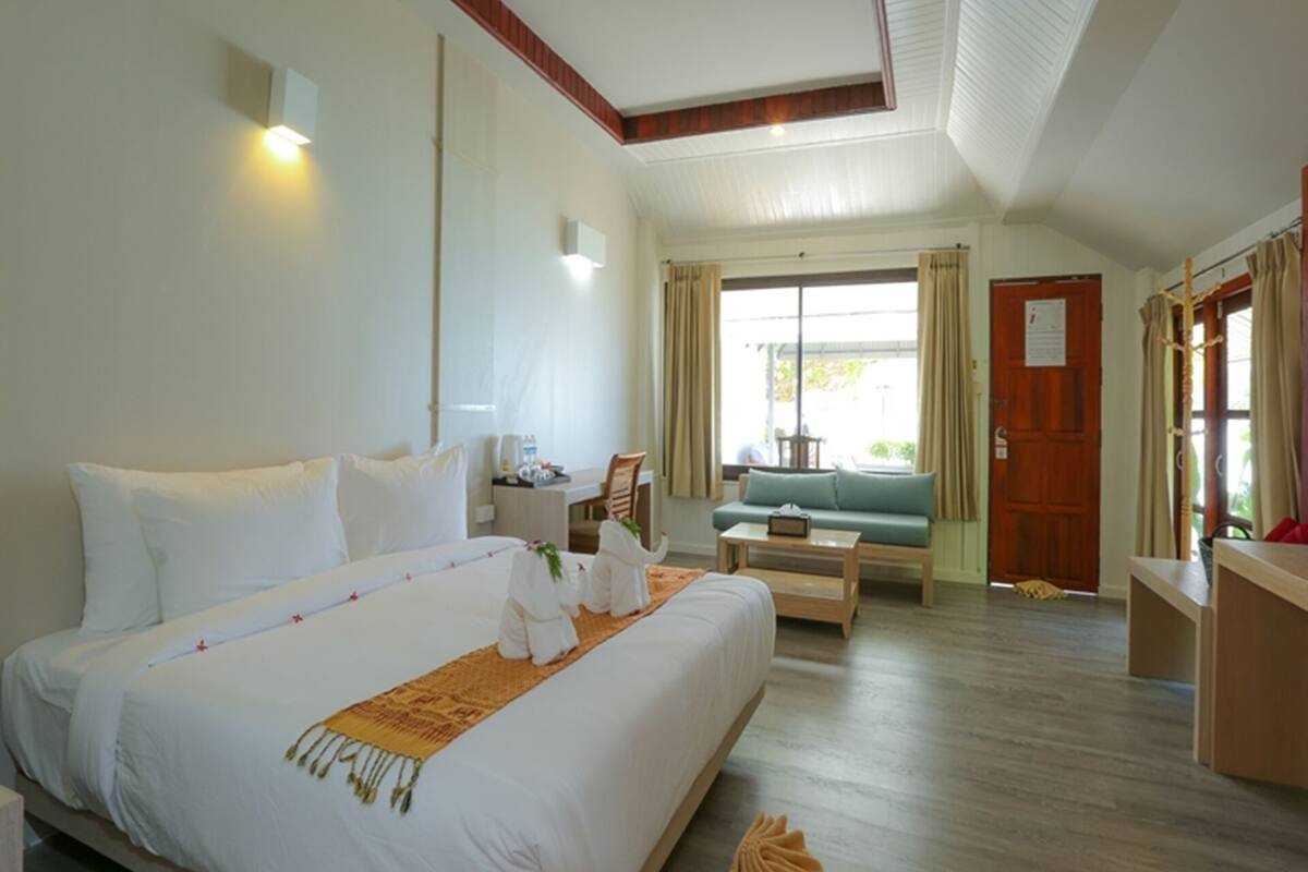 A hotel room with a large bed, a small sofa, a wooden coffee table, and a desk with a chair.
