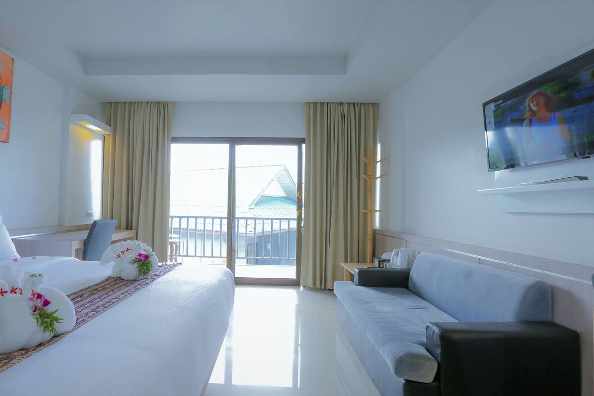 A hotel room with a bed, a sofa, a TV, and a balcony with a view.