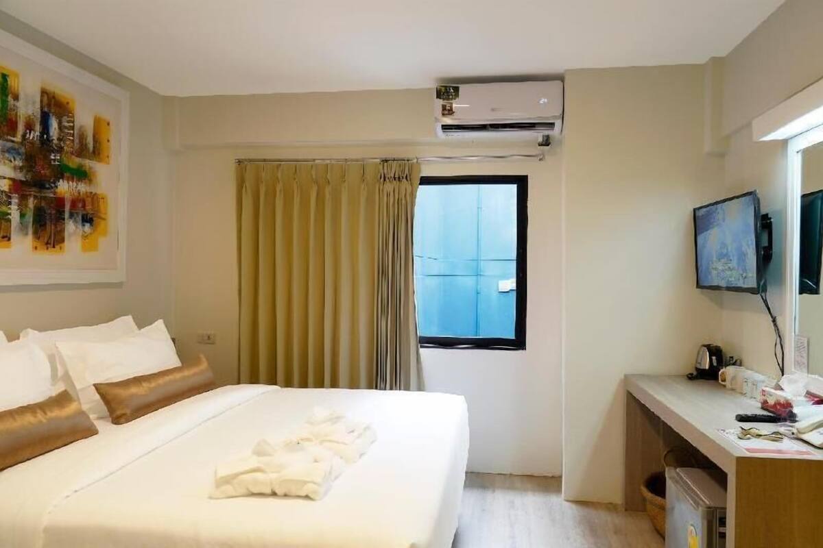 A hotel room with a bed, a desk, an air conditioner, a window with curtains, and a television.