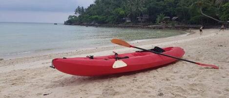 Un kayak rouge sur une plage de sable, avec une colline boisée en arrière-plan.