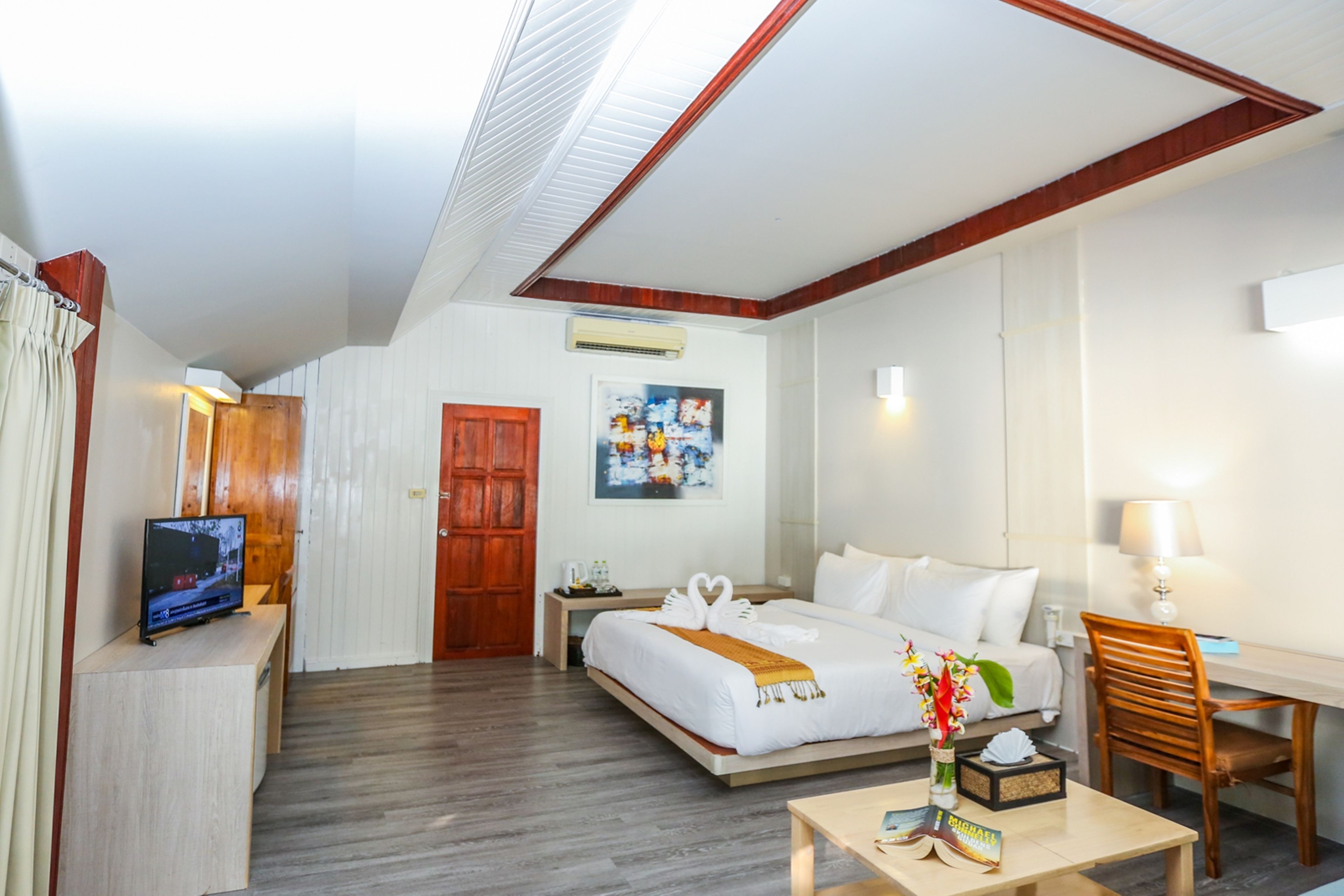 Hotelkamer met een bed, nachtkastje, televisie, bureau, stoel en een schilderij aan de muur.