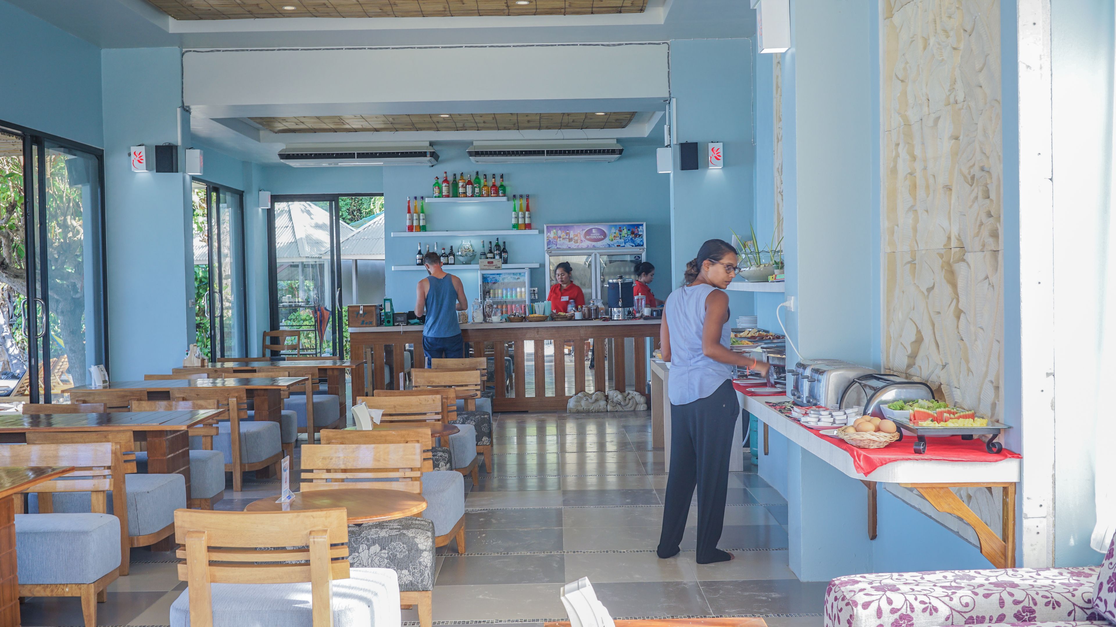 Un restaurante con mesas y sillas de madera, una barra de buffet con comida y una zona de bar.
