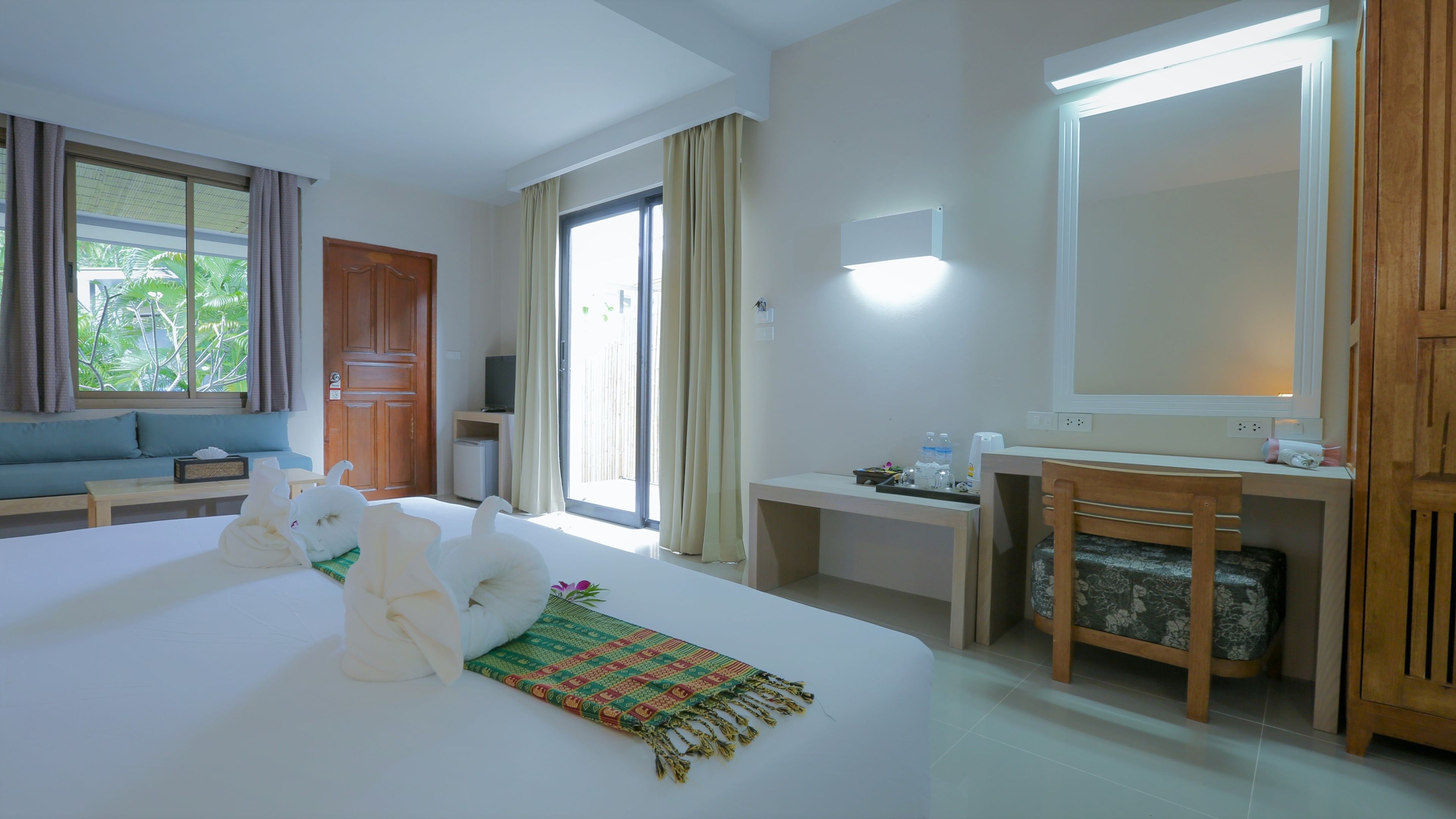 A hotel room with a bed, a sofa, a desk, a mirror, and a television.