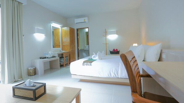 A hotel room with a large bed, a desk with a chair, a small table, and a mirror.