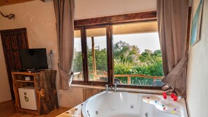 Une chambre dotée d’une grande baignoire, de meubles en bois, d’une télévision et d’une fenêtre donnant sur un paysage verdoyant.