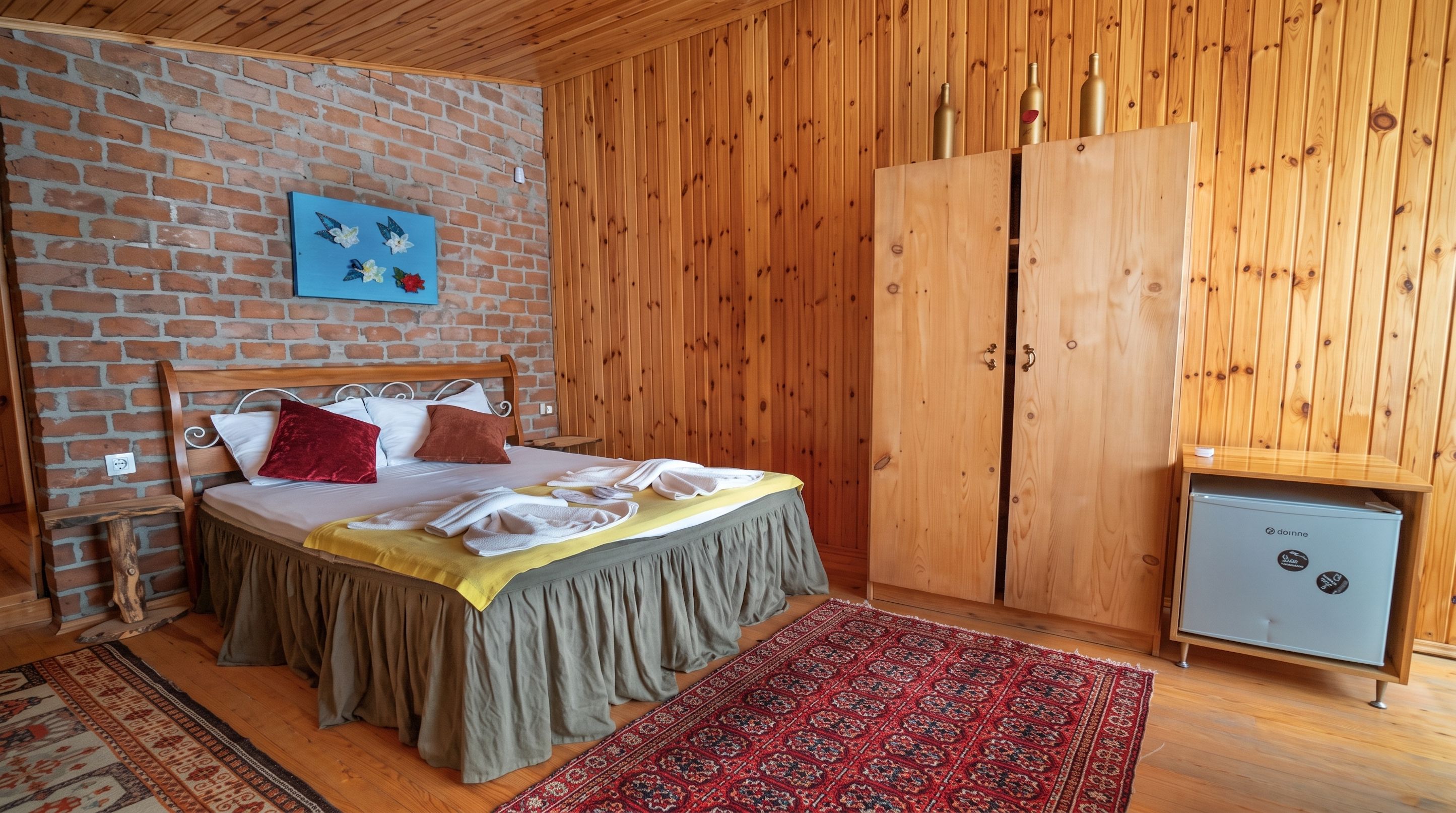 A room with a bed, a wooden wardrobe, a small fridge, and a patterned rug.