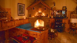 Une pièce chaleureuse avec une cheminée en pierre, des meubles en bois et une bibliothèque remplie de livres et d’objets décoratifs.