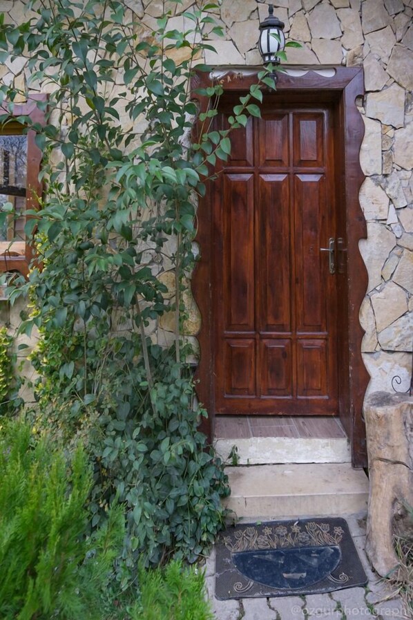 Una puerta de madera con un muro de piedra, un escalón que lleva a ella y un felpudo con motivos florales.