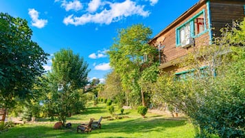 A wooden house with a garden, a lawn, and a clear blue sky.