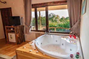 A room with a large bathtub, wooden furniture, a television, and a window with a view of greenery. - Agva Masal Evi (Sile)