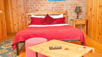 Una habitación con una cama de madera, una mesita pequeña, una mesita de noche y una pared de ladrillo.