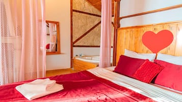 Un dormitorio con cabecera de madera, cama con ropa de cama roja, toalla blanca y una decoración con forma de corazón.