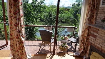 Un balcón con mobiliario de mimbre y una planta en maceta, con vistas a un paisaje verde exuberante y una masa de agua.
