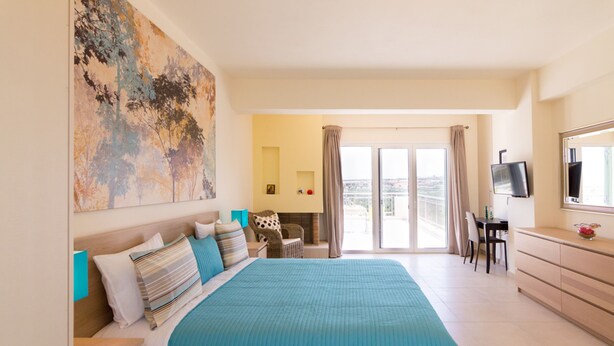 Une chambre d’hôtel avec un grand lit, un bureau avec une chaise, une télévision et un balcon avec des rideaux.