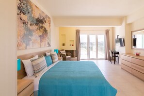 A hotel room with a large bed, a desk with a chair, a television, and a balcony with curtains.