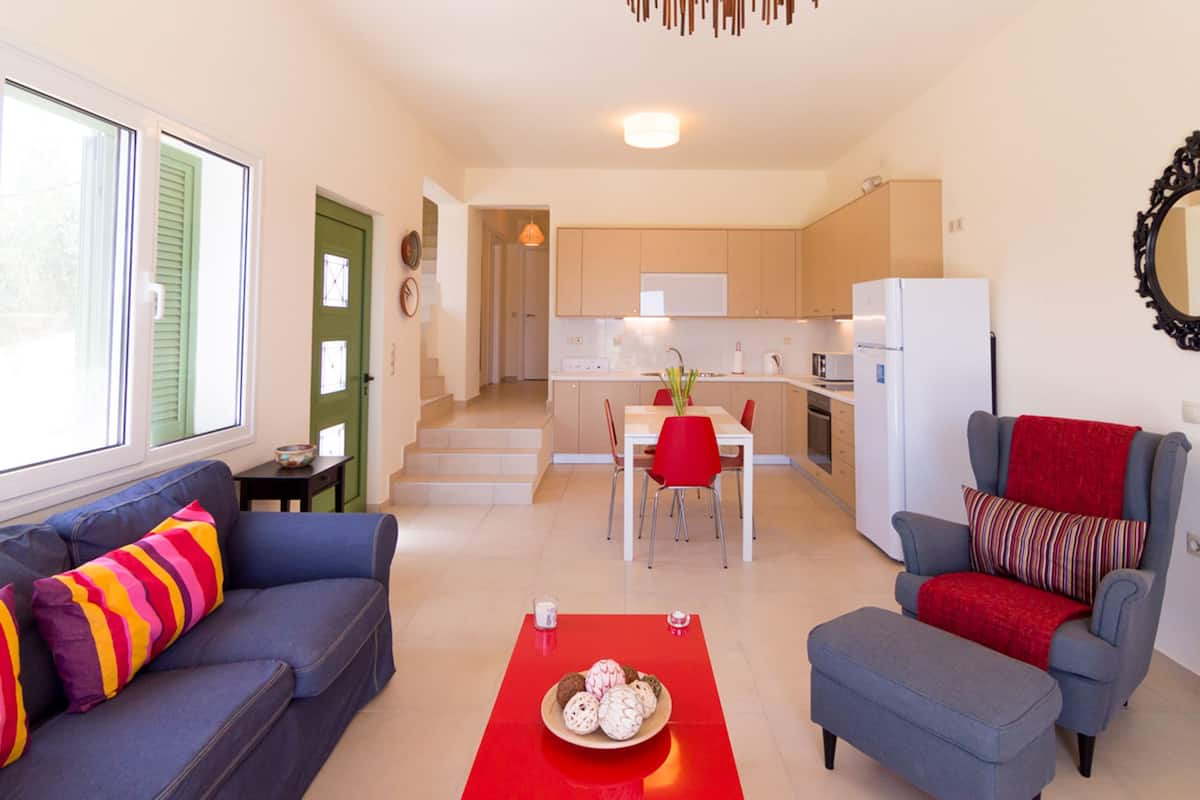 Een moderne woonkamer met een bank, een rode ottoman en een eethoek met een tafel en stoelen.