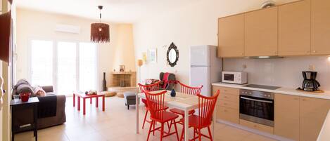 A modern kitchen with a dining area, featuring a white table, red chairs, a microwave, and a coffee maker.