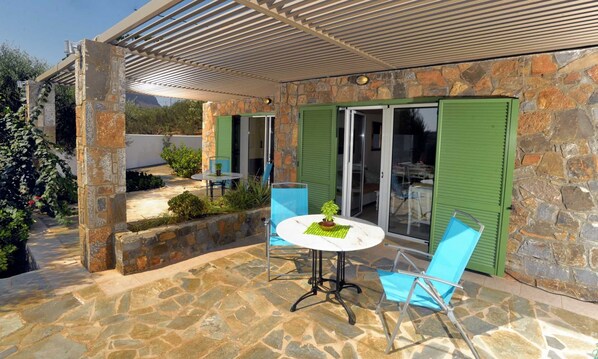 A patio with stone flooring, a round table, two chairs, and a potted plant.