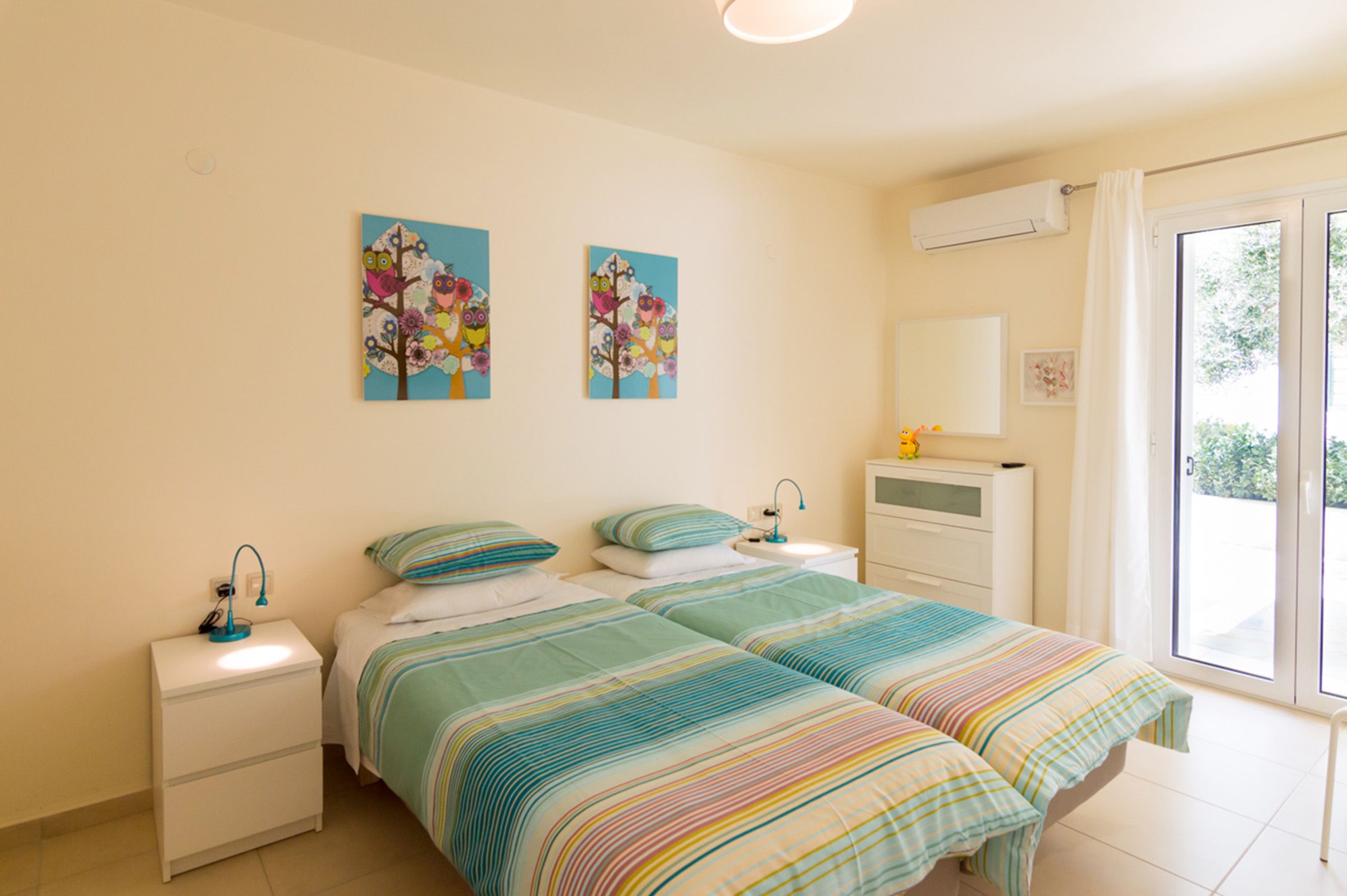 Een slaapkamer met twee bedden, een nachtkastje, een spiegel en een raam met uitzicht op groen.