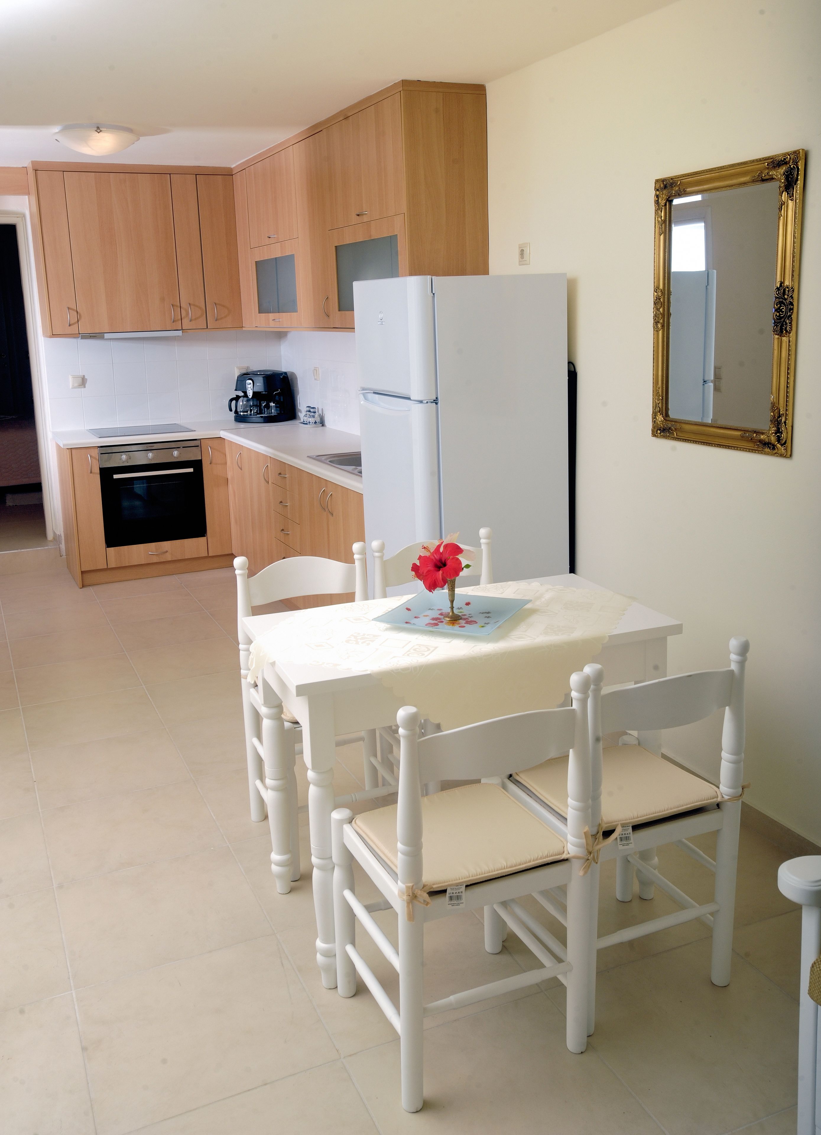 A compact kitchen with wooden cabinets, a white refrigerator, and a dining table with white chairs.