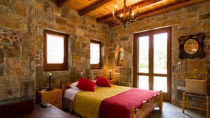 Une chambre aux murs de pierre, avec un lit en bois, des oreillers rouges et un lustre.
