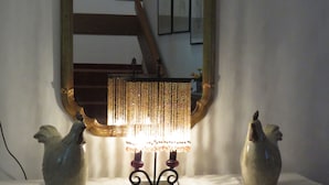 Un miroir avec un cadre décoratif, une lampe allumée et deux figurines de coqs en céramique posées sur une table.