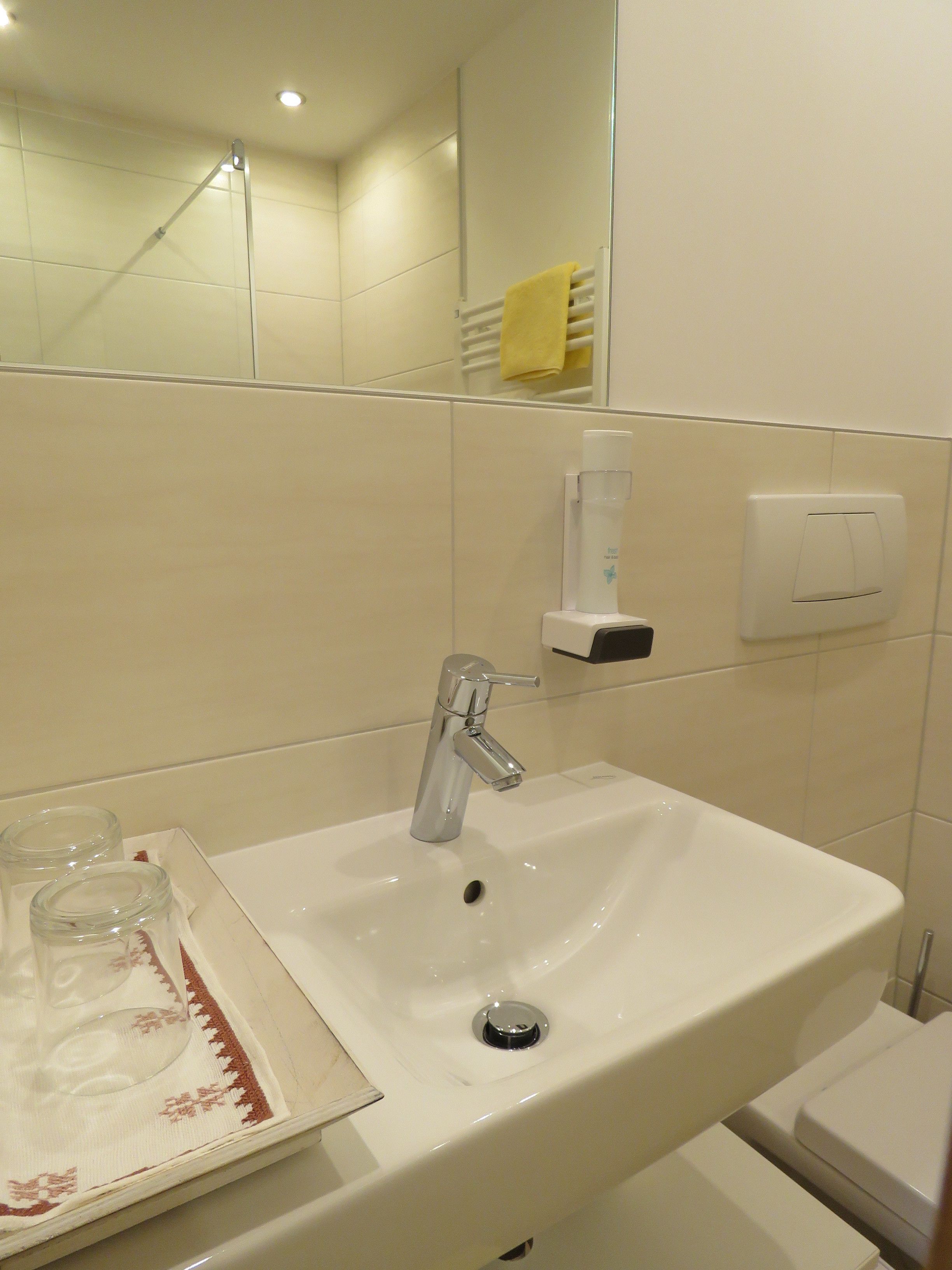 Un baño con lavamanos blanco, espejo y toallero.
