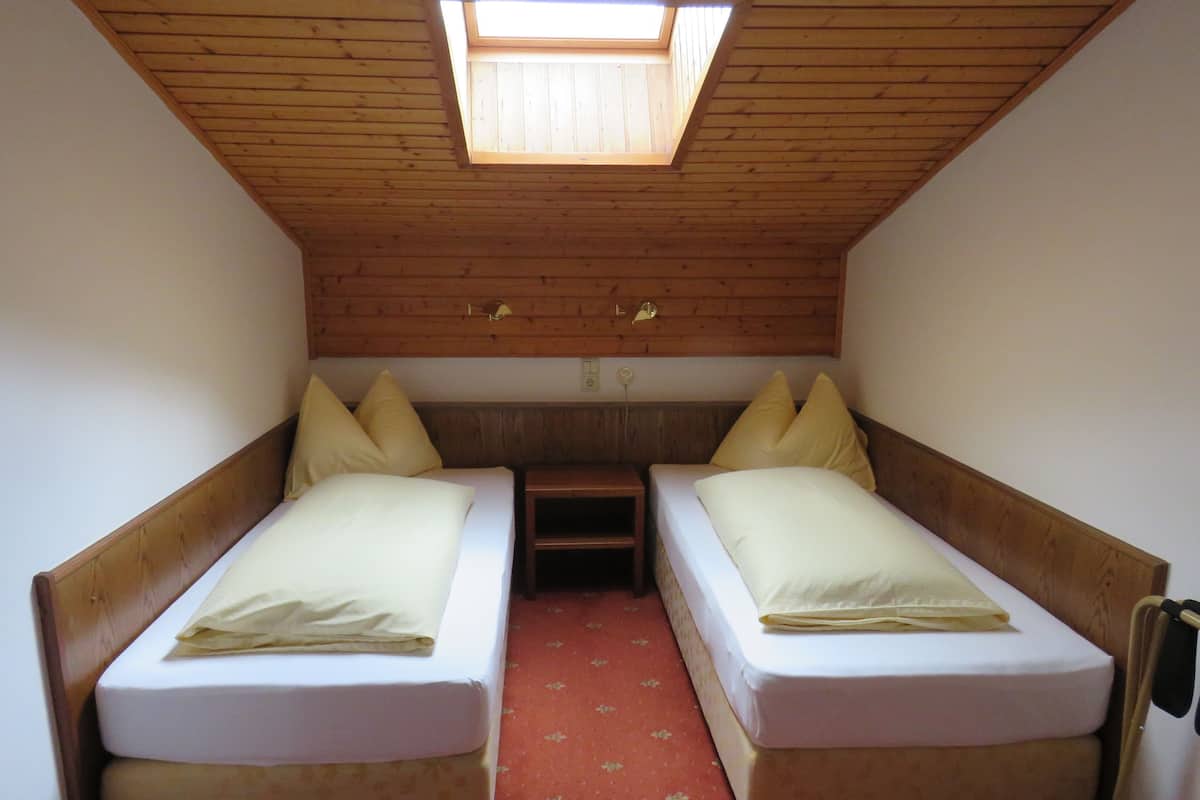 Una habitación pequeña y acogedora con dos camas individuales, techo de madera y tragaluz.