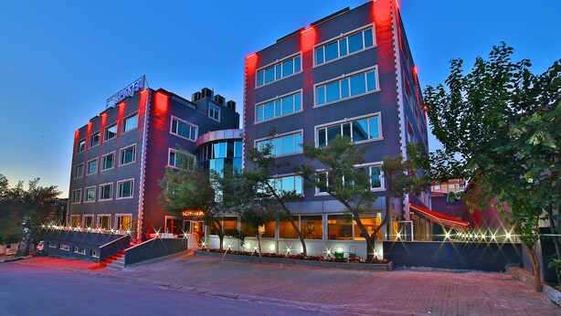 Un hotel de varios pisos con diseño moderno, que destaca por una entrada imponente con un espacio de estar al aire libre techado y una fachada bien iluminada.